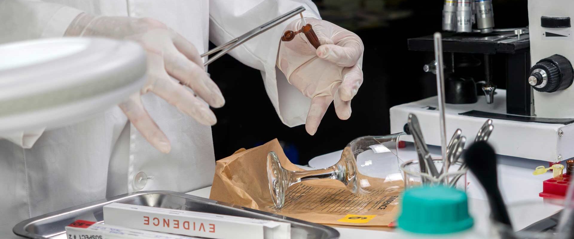 forensics expert works to collect evidence from a wine glass and other items in a lab setting